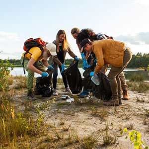 Group cleaning litter near lake, collecting trash in nature
