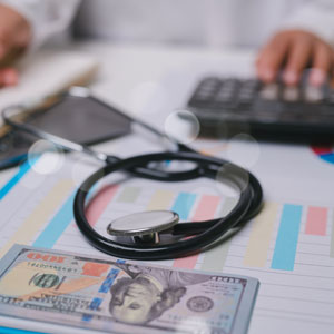 Stethoscope, dollar bills, and a calculator on a chart, symbolizing healthcare costs.