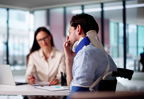 Injured man in neck brace and wheelchair consults female personal injury lawyer.